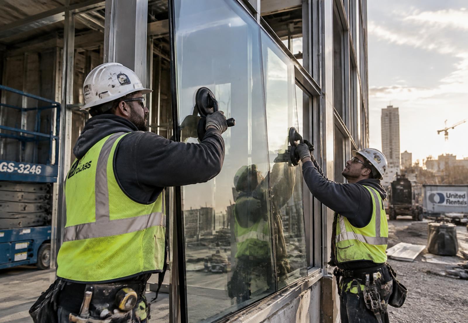 Two glaziers in hard hats setting a glass panel into a storefront frame