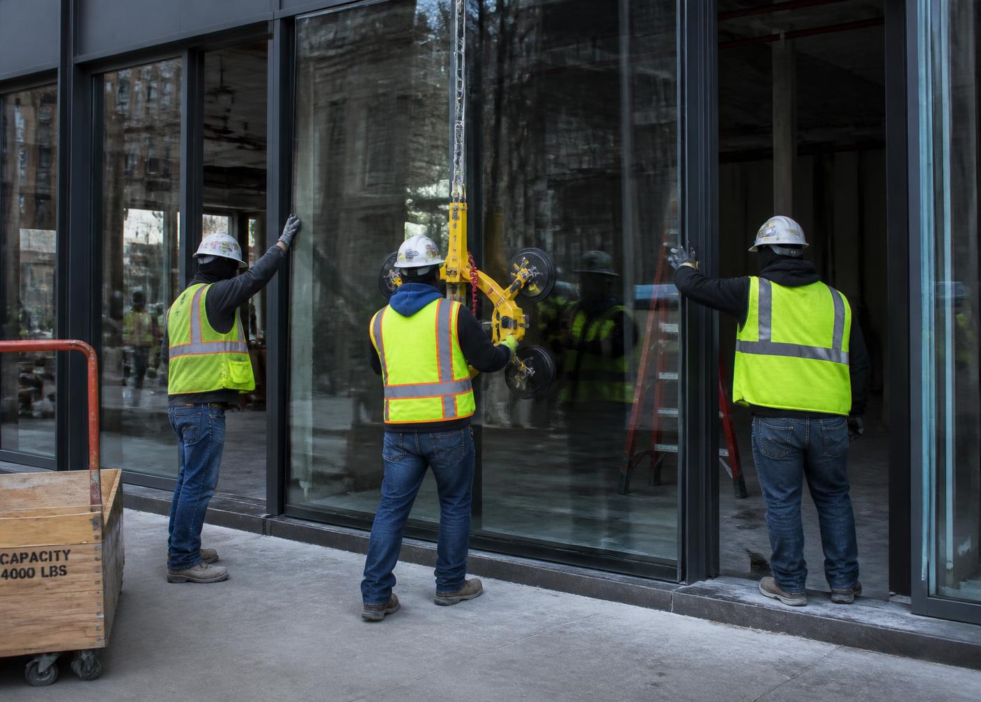 Commercial glazing crew positioning a large storefront glass panel with suction equipment